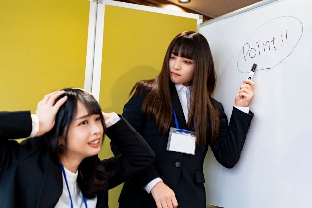 植毛手術前に確認すべき重要ポイントを見逃し、頭を抱える女性と、ホワイトボードを指して注意喚起する同僚。費用や痛み、仕上がりに関する事前確認の大切さをユーモラスに表現した場面。質問は聴くべし。