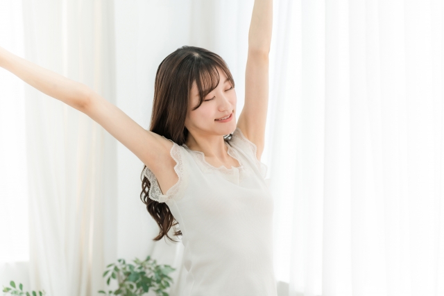 背中まで伸びたロングヘアの女性が両腕を伸ばしてストレッチする姿。頭頂部に軽度の薄毛が見られるが、通常は目立たない程度。女性にも適応される自毛植毛治療の可能性を示唆するイメージ