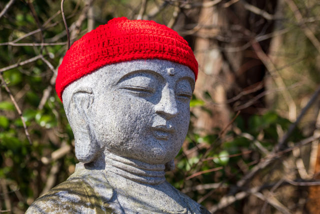 赤いニット帽をかぶった石造りの童子像。帽子が脱毛の原因とされる俗説を象徴的に表現したイメージカット。