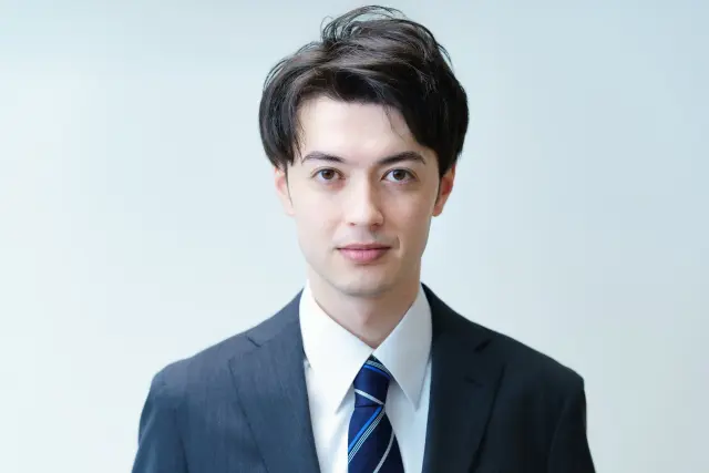 薄毛の初期サインに気づきつつも、不安と希望の間で揺れる若い日本人ビジネスマンの表情。自分に合った治療法を探して悩む20代男性が、AGAや若年性脱毛への迷いを抱えながらも前向きな笑顔を見せている様子。
