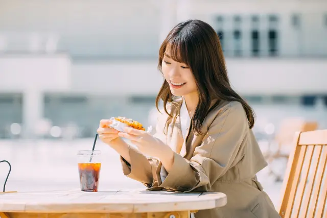 屋外カフェでスイーツを手に微笑む女性。かつての薄毛の悩みから解放され、今は自然体で外出を楽しめるようになった様子が伝わる