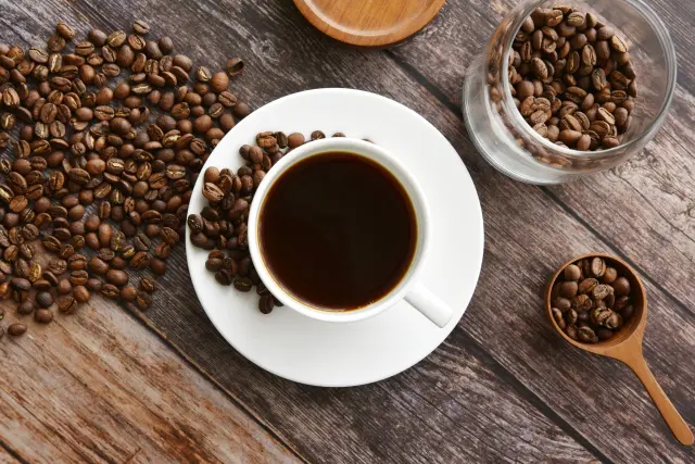 白いカップに注がれたブラックコーヒーと大量のコーヒー豆の演出｜コーヒーベリー由来のカフェインや抗酸化成分の美容・育毛効果を紹介するヒロクリニック公式コラム用イメージ