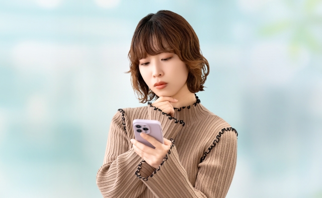 スマートフォンの画面を見ながら不安そうに悩む女性のイメージ｜海外植毛の詐欺被害や闇クリニックを見抜く判断力の重要性を象徴するストック写真