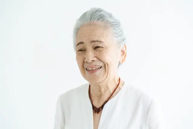 白髪の高齢女性が遠くを見つめながらほほえみを浮かべている様子。年齢を重ねた自分自身を受け入れつつも、見た目の変化に前向きな気持ちを持つ姿を描写し、白髪でも植毛による選択肢があるというメッセージと共鳴するイメージ。