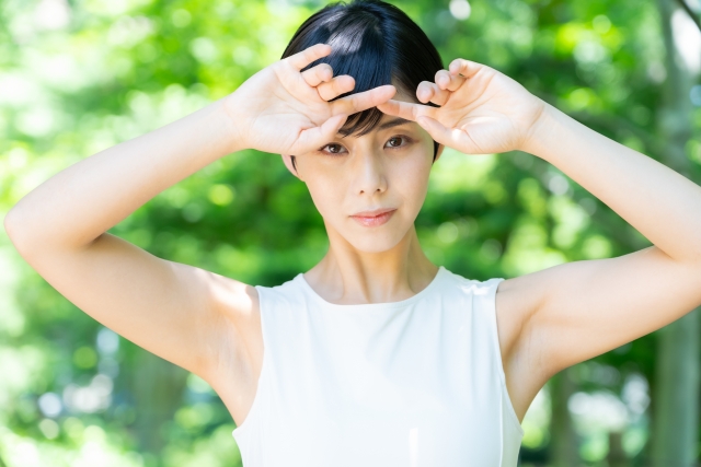 強い日差しを手で遮る女性。黒く艶のある髪と白い肌のコントラストは、日本人特有の太く色素の濃い直毛の特徴を示す印象的なビジュアル。