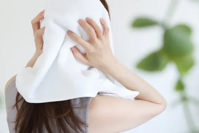 シャンプー後にタオルで髪の水分をやさしく拭き取る女性のイメージ。正しい洗髪後のヘアケア手順として、ドライヤー前に髪の毛の水分をしっかり吸収する様子を表現。