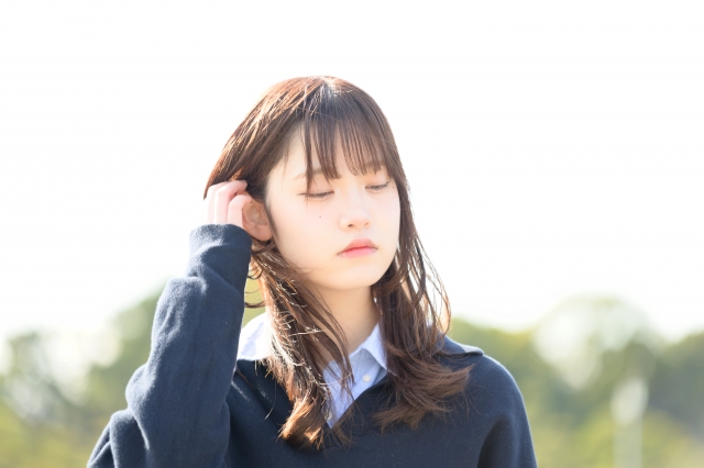 日差しを浴びながら髪を耳にかける女子高校生。健康的な髪のツヤが印象的で、思春期のヘアケアや将来の抜け毛予防の大切さを感じさせるシーン。女性の髪の悩みに寄り添う医療コラム用イメージ
