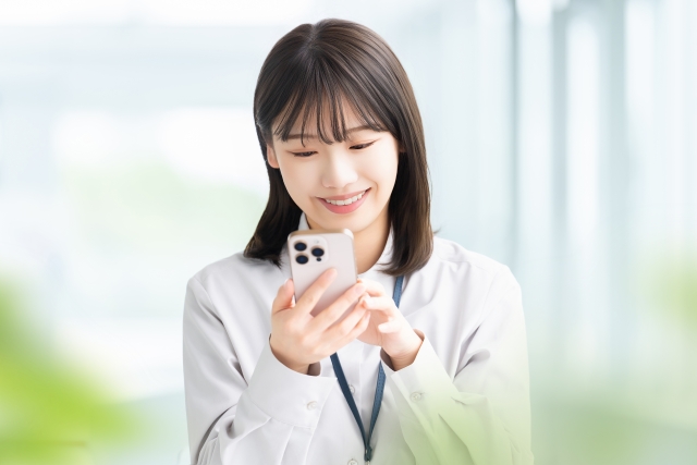 スマートフォンで髪に関する最新ニュースを読んで微笑む若い女性のストック画像。世界の毛髪専門医によるシャキーラの美髪選出や、薄毛治療の新技術に関心を寄せる読者像をイメージした写真。
