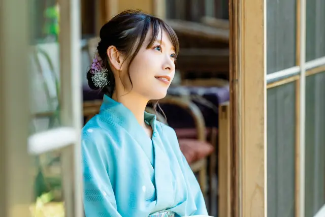 淡い空色の着物をまとい、明るい表情で空を見上げる若い和装の日本人女性。整えられた髪と透明感のある肌が印象的で、自然由来の美容成分による内面と外見の調和、美と健康の関係性を象徴するビジュアル。