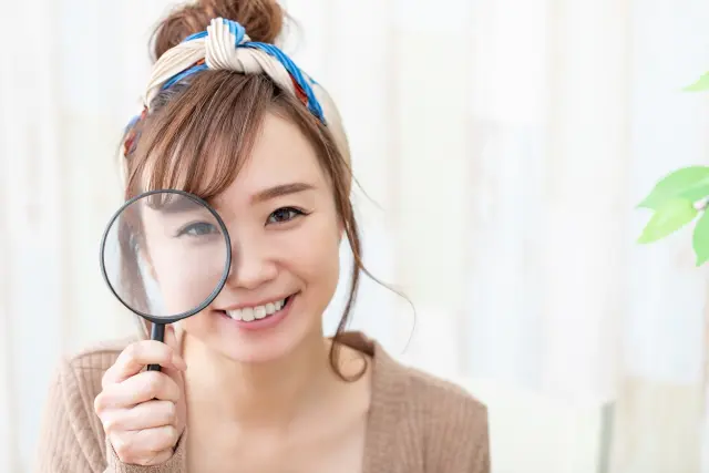 植毛手術を検討する際に重要な疑問や見落としがちなポイントをじっくり確認するイメージを表現した虫眼鏡を持つ笑顔の女性。費用や痛みに関する注意点を深掘りする象徴的なシーン。