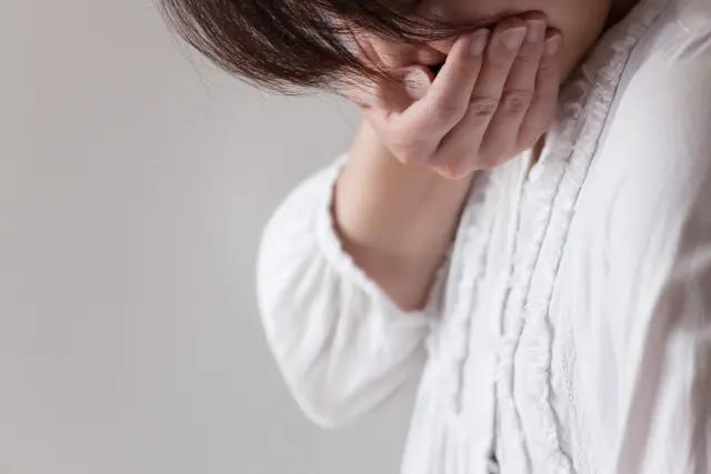口元を手で覆い、髪が目元を隠す女性の顔のクローズアップ。急激な抜け毛に悩み、産後や更年期に起こる女性の薄毛による気分の落ち込みを象徴する暗い表情