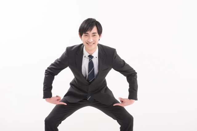 満足げな表情のビジネスマンが両手で股間を指さし、性機能への自信を表現している様子。AGA治療薬フィナステリドの副作用や性機能への影響について扱う記事の文脈に関連したイメージ