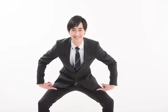 満足げな表情のビジネスマンが両手で股間を指さし、性機能への自信を表現している様子。AGA治療薬フィナステリドの副作用や性機能への影響について扱う記事の文脈に関連したイメージ