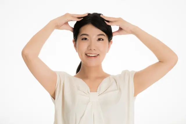 薄毛治療を前向きに捉える若い女性が、明るい笑顔で髪の横に手を添えてポーズをとっている様子。植毛手術や薄毛治療が恥ずかしいことではないというメッセージを体現｜薄毛治療の社会的受容に関するコラム用画像