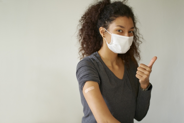 明るい表情で「大丈夫」のジェスチャーを見せるアフリカ系の女性。象徴的なカールのある豊かな天然ヘアスタイルが印象的で、黒人女性の文化的なヘアアイデンティティや自信を感じさせる一枚。脱毛に悩みながらも前向きに髪と向き合う姿勢を象徴している。