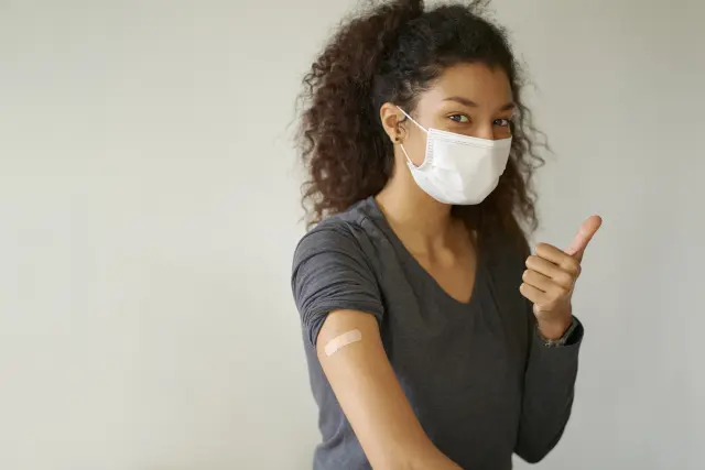 明るい表情で「大丈夫」のジェスチャーを見せるアフリカ系の女性。象徴的なカールのある豊かな天然ヘアスタイルが印象的で、黒人女性の文化的なヘアアイデンティティや自信を感じさせる一枚。脱毛に悩みながらも前向きに髪と向き合う姿勢を象徴している。