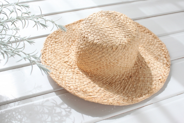 白樺のベンチに置かれた麦わら帽子の静かな情景。がん治療中の患者が外出時に感じる季節のぬくもりや、外見への配慮と自然とのつながりを象徴するイメージ。