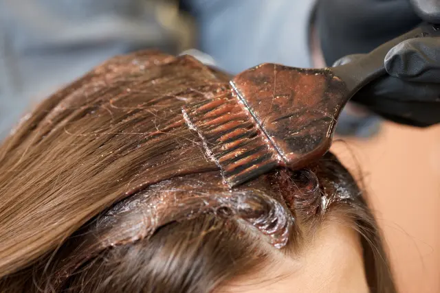 ブリーチやカラーリングによる髪の損傷リスクを象徴する、ブラウンのヘアブラシで染料を塗布する施術中の様子。毛髪内部に薬剤が浸透する工程をイメージしたイラスト。