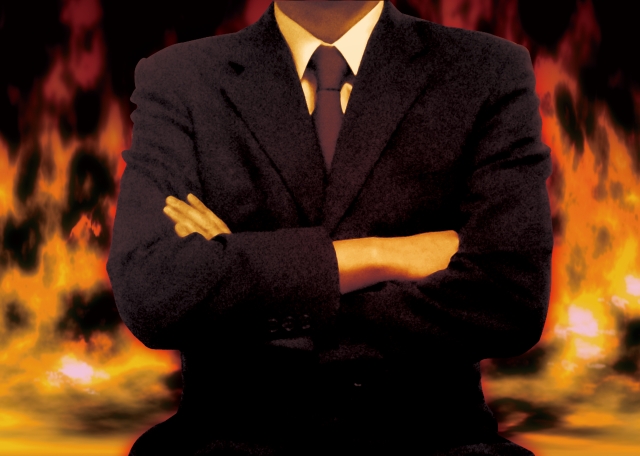 違法植毛を行うブラックマーケット型クリニックの危険性や不透明な実態を象徴する、赤い炎を背景に腕を組むビジネスマンのイメージ