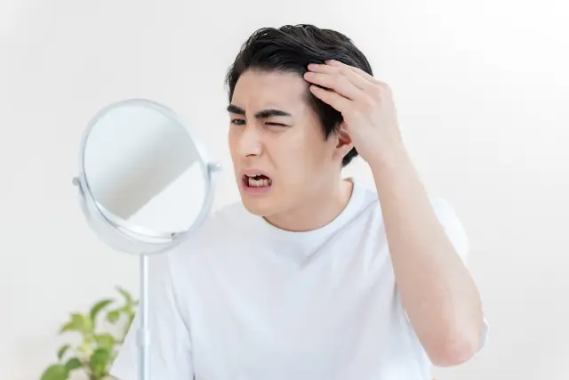 鏡で生え際を見る男性