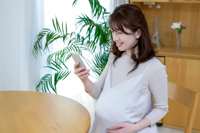 妊娠の報告をスマホで嬉しそうにしている妊婦
