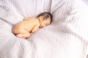 シーツ上に丸くなって寝る赤ちゃん