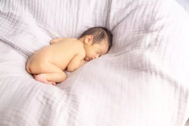 シーツ上に丸くなって寝る赤ちゃん