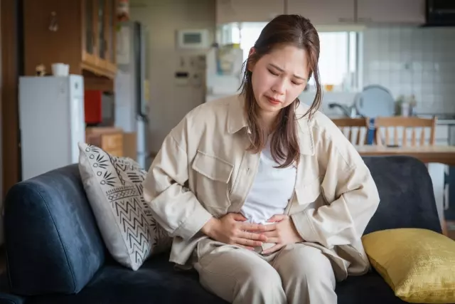 部屋でお腹が痛く手を当てる女性